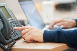 Reliable IT Support - Person using a telephone with their left hand and a laptop with their right.