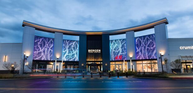 Shopping center entrance featuring large transparent LED façade displays with animated blue and purple graphics mounted across the exterior of a modern retail complex.