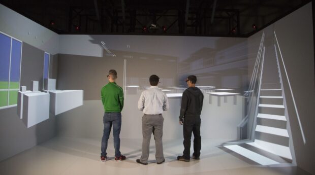 Wichita State CAVE for AEC walkthrough. 3 men standing in immersive space looking at a building design rendering